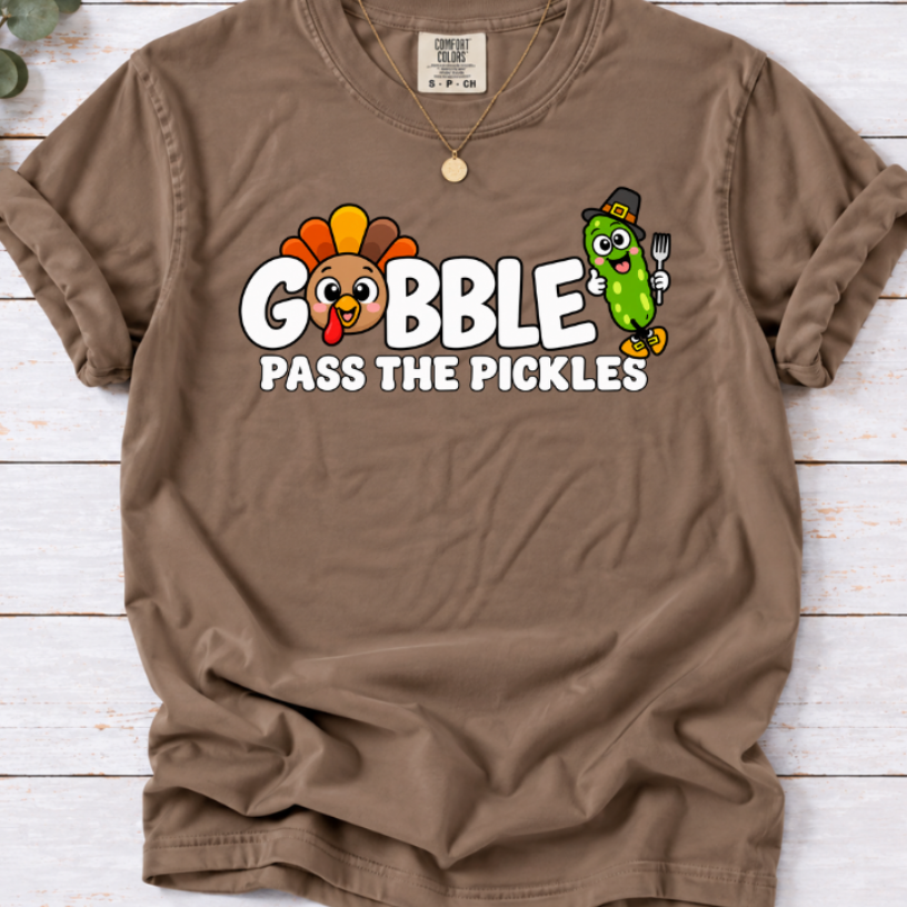 Espresso brown T-shirt with ‘Gobble Pass the Pickles’ lettering, a cartoon turkey and a pilgrim pickle holding a fork.