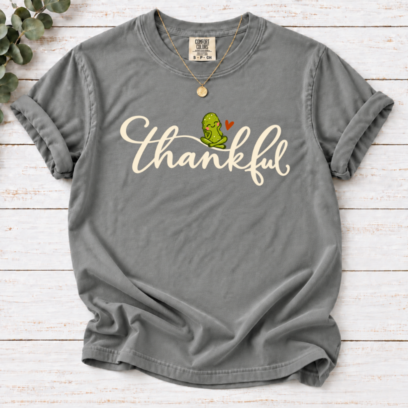 Grey T-shirt with thankful script, a smiling green pickle, and a small orange heart.