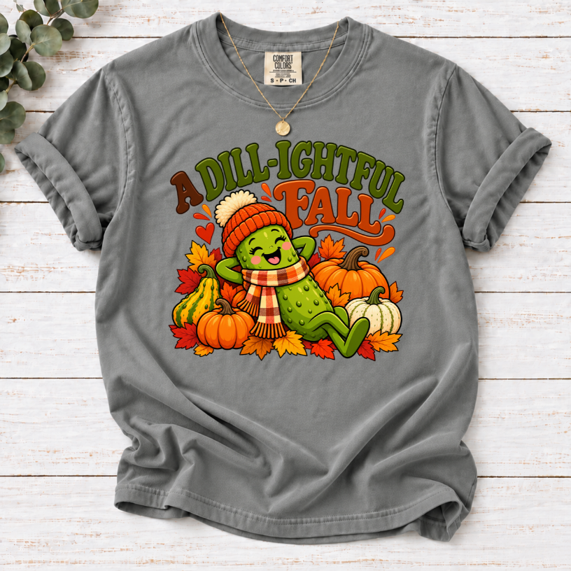 Grey A Dill-ightful Fall T-shirt with a smiling pickle in a beanie and plaid scarf among pumpkins and autumn leaves.