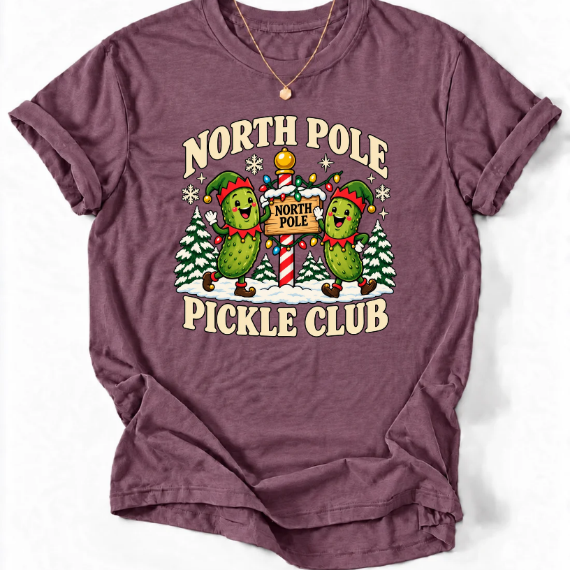 Heather Maroon T-shirt with “North Pole Pickle Club” lettering and two pickle elves beside a candy cane signpost and snowy trees.