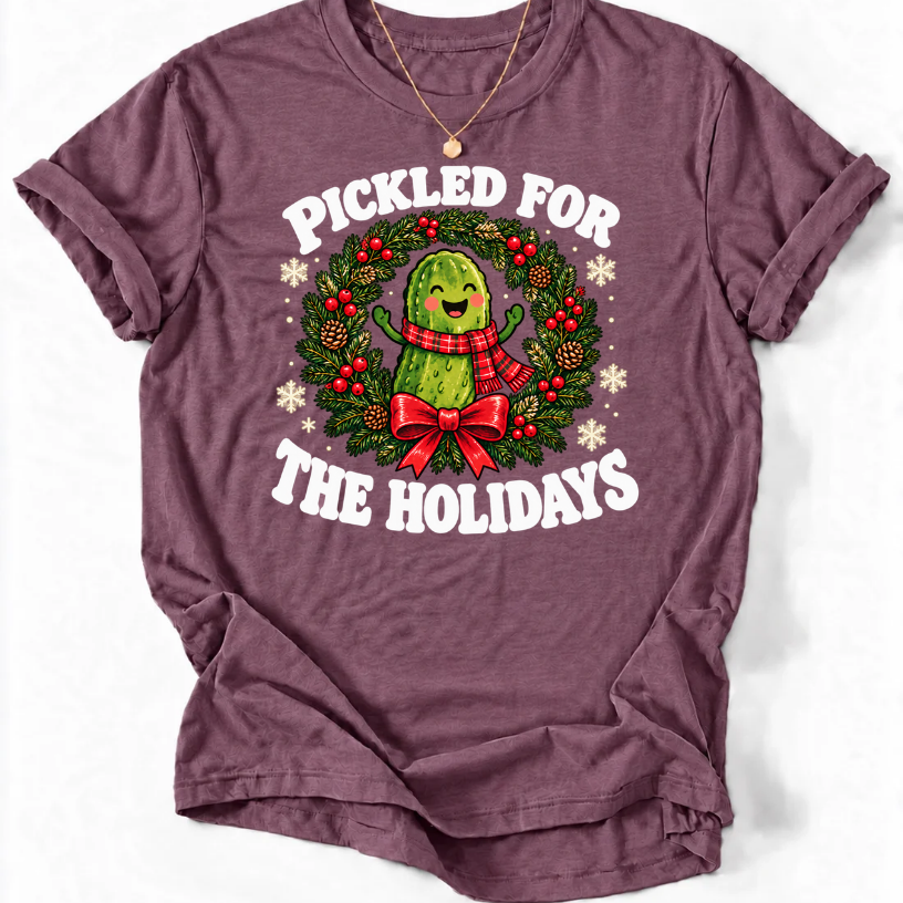 Heather Maroon Pickled for the Holidays’ T-shirt with a smiling pickle in a red scarf inside a Christmas wreath.”