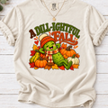 Ivory A Dill-ightful Fall T-shirt with a smiling pickle in a beanie and plaid scarf among pumpkins and autumn leaves.