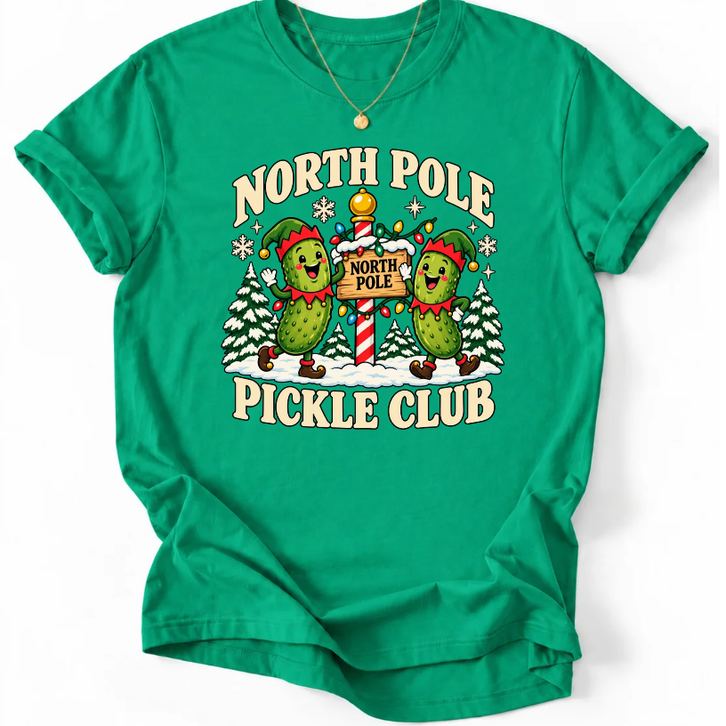 Kelly Green T-shirt with “North Pole Pickle Club” lettering and two pickle elves beside a candy cane signpost and snowy trees.