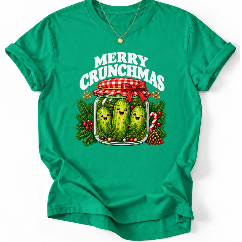 Krelly Green T-shirt with “Merry Crunchmas” lettering above three smiling pickles in a jar decorated with a red bow and Christmas greenery.