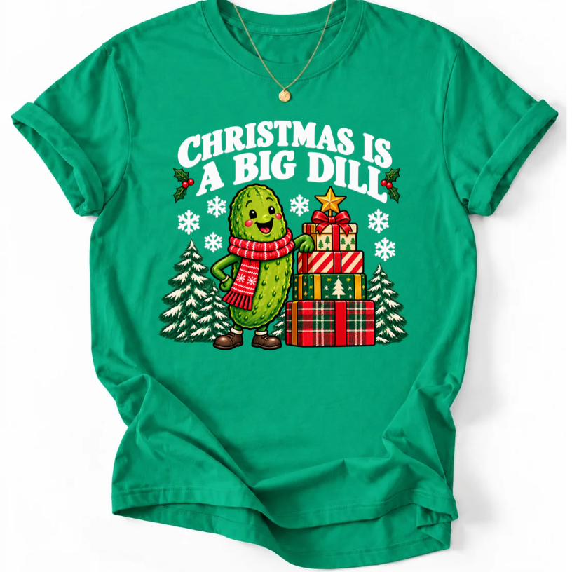 Kelly Green T-shirt with “Christmas Is a Big Dill” lettering and a smiling pickle in a red scarf beside stacked gifts and snowy trees.