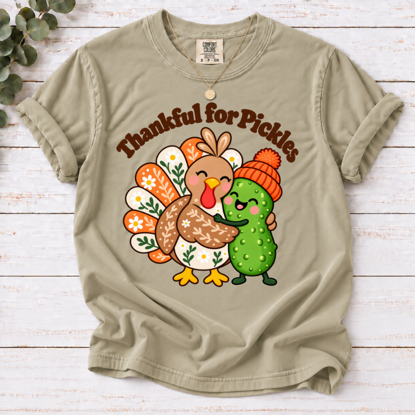 khaki  Thankful for Pickles T-shirt featuring a cartoon turkey hugging a green pickle wearing an orange knit hat.”