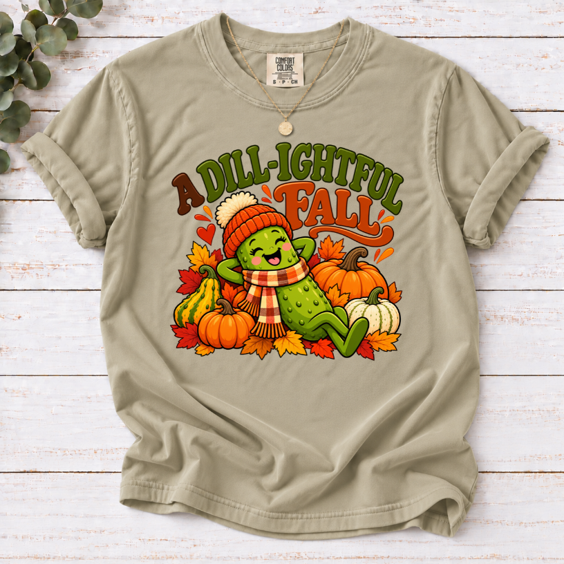 Khaki A Dill-ightful Fall T-shirt with a smiling pickle in a beanie and plaid scarf among pumpkins and autumn leaves.