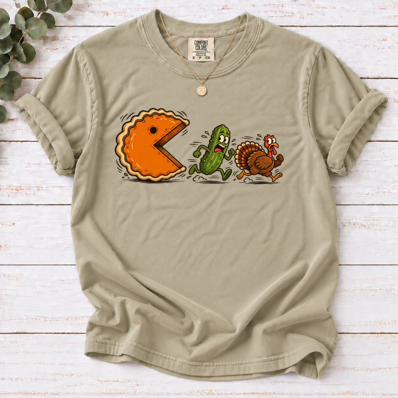 Khaki T-shirt featuring a cartoon pumpkin pie chasing a frightened pickle and turkey.