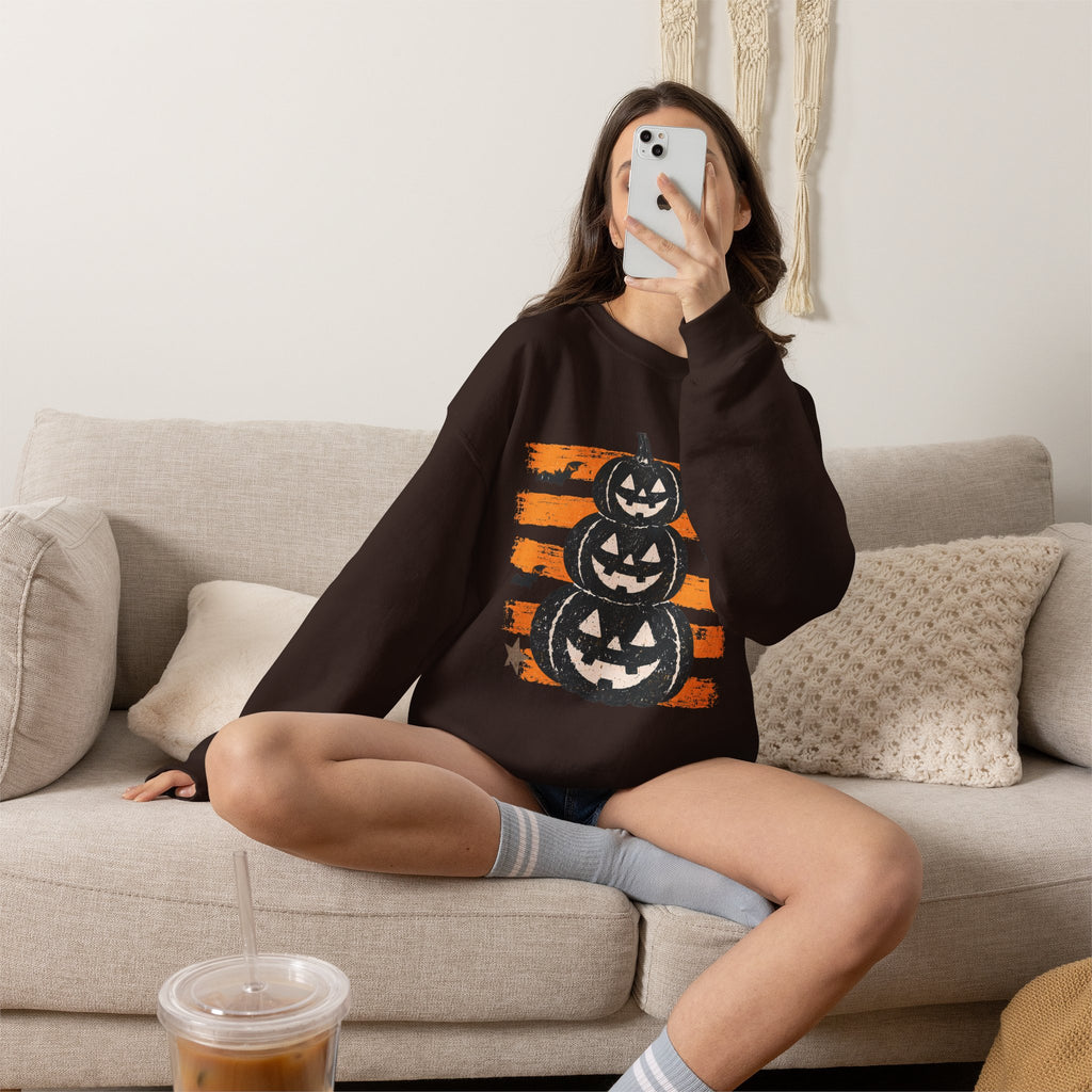 A woman sits cross-legged on a beige couch taking a mirror selfie while wearing a dark brown oversized sweatshirt with a graphic print of a cowboy boot and the text 'TOME UN COWBOY'.