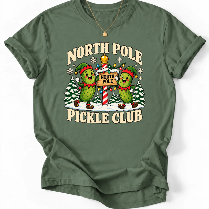 Military Green T-shirt with “North Pole Pickle Club” lettering and two pickle elves beside a candy cane signpost and snowy trees.