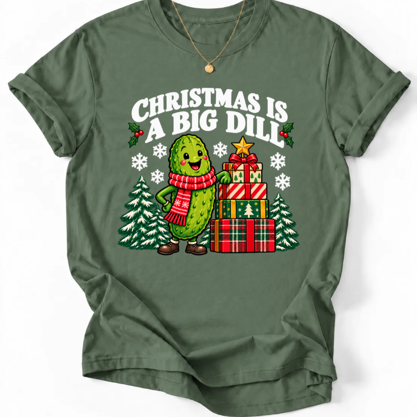 Military Green T-shirt with “Christmas Is a Big Dill” lettering and a smiling pickle in a red scarf beside stacked gifts and snowy trees.