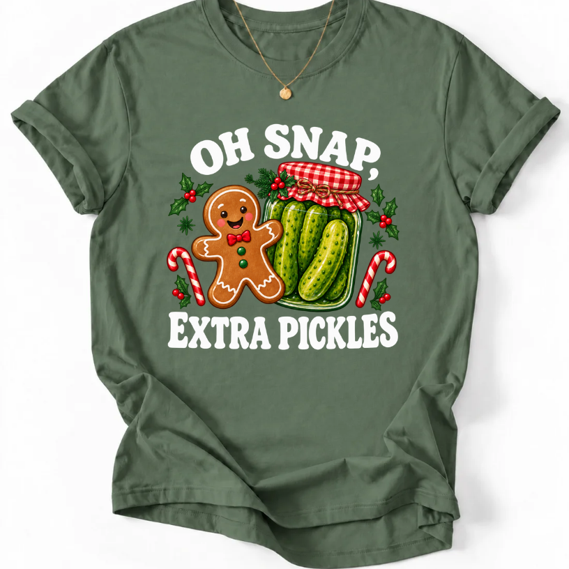 Military Green T-shirt with “Oh Snap, Extra Pickles” lettering, a smiling gingerbread character, and a pickle jar surrounded by candy canes and holly.