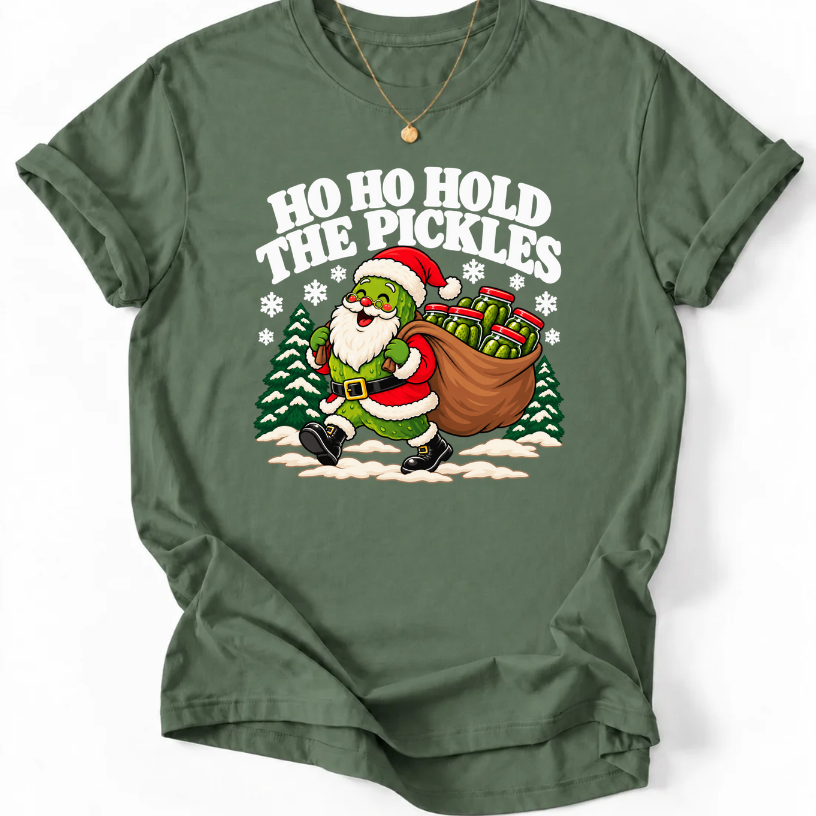 Military Green T-shirt with “Ho Ho Hold the Pickles” lettering and a pickle dressed as Santa carrying a sack of pickle jars beside snowy trees.
