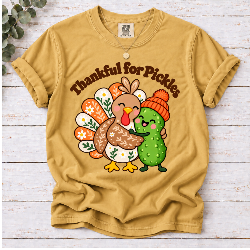 mustard Thankful for Pickles T-shirt featuring a cartoon turkey hugging a green pickle wearing an orange knit hat.”