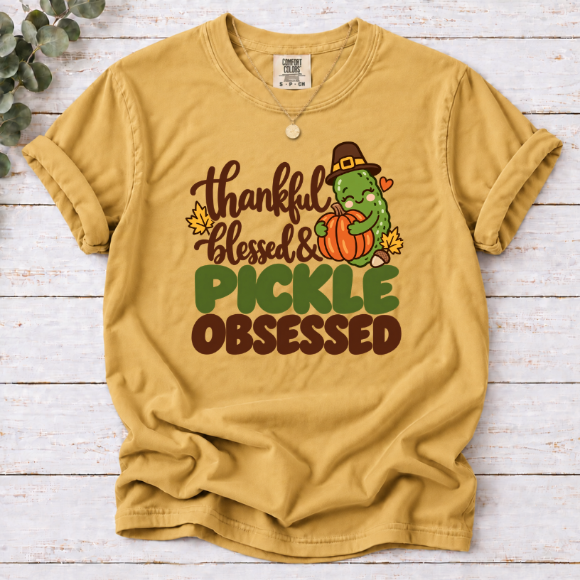 mustard T-shirt with ‘Thankful Blessed & Pickle Obsessed’ lettering and a pilgrim-hat pickle hugging a pumpkin