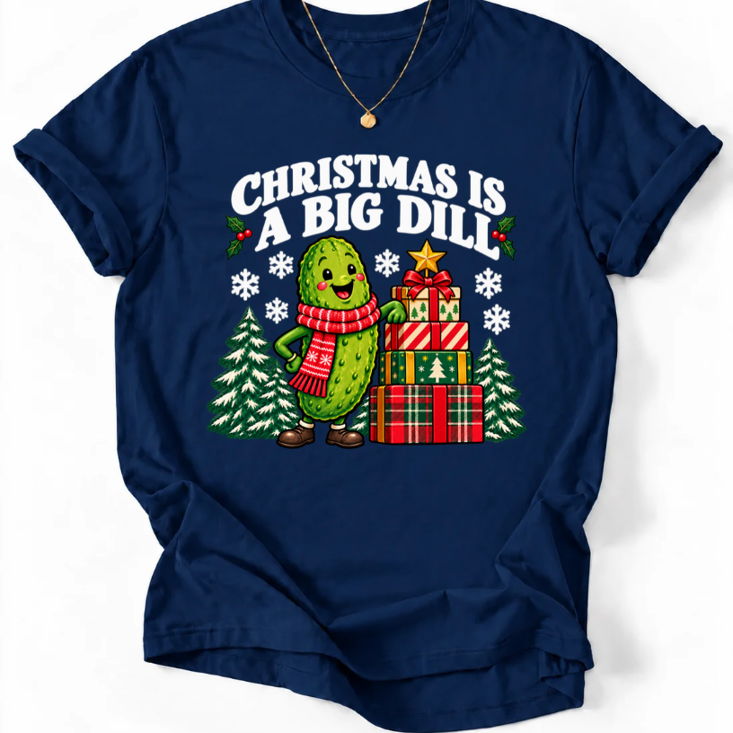 Navy T-shirt with “Christmas Is a Big Dill” lettering and a smiling pickle in a red scarf beside stacked gifts and snowy trees.