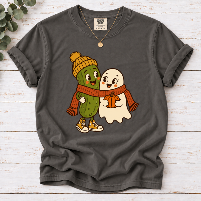 pepper T-shirt featuring a smiling pickle in a yellow beanie beside a ghost holding a pumpkin, sharing an orange scarf.”