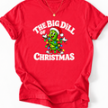 Red T-shirt with ‘The Big Dill of Christmas’ text and a smiling pickle in a Santa hat wrapped in colorful lights.”