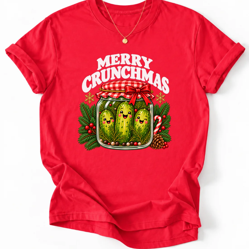 Red T-shirt with “Merry Crunchmas” lettering above three smiling pickles in a jar decorated with a red bow and Christmas greenery.
