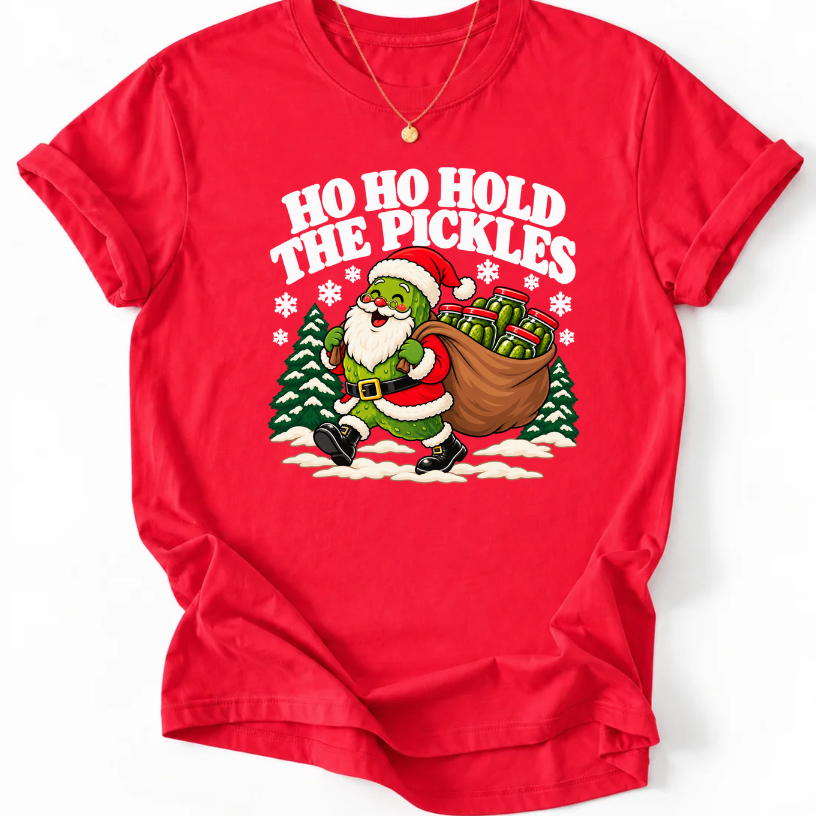 Red T-shirt with “Ho Ho Hold the Pickles” lettering and a pickle dressed as Santa carrying a sack of pickle jars beside snowy trees.