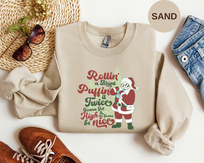 A beige crewneck sweatshirt laid flat on a white surface, featuring a colorful Christmas graphic with the text 'Rollin' a Whist Puffin It Twices Gonna Get High it won't be nice' 