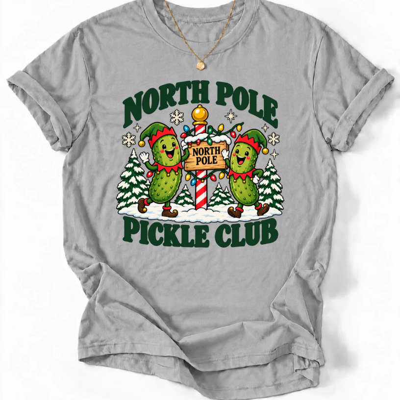 Sports Grey T-shirt with “North Pole Pickle Club” lettering and two pickle elves beside a candy cane signpost and snowy trees.