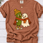 Yam-colored T-shirt featuring a smiling pickle in a yellow beanie beside a ghost holding a pumpkin, sharing an orange scarf.