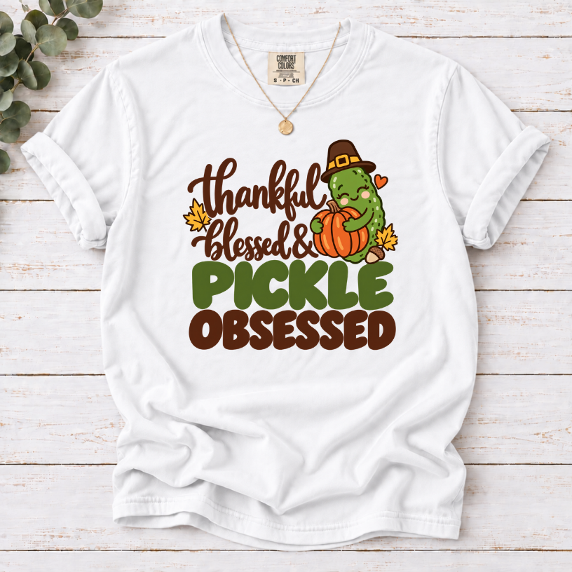 White T-shirt with ‘Thankful Blessed & Pickle Obsessed’ lettering and a pilgrim-hat pickle hugging a pumpkin